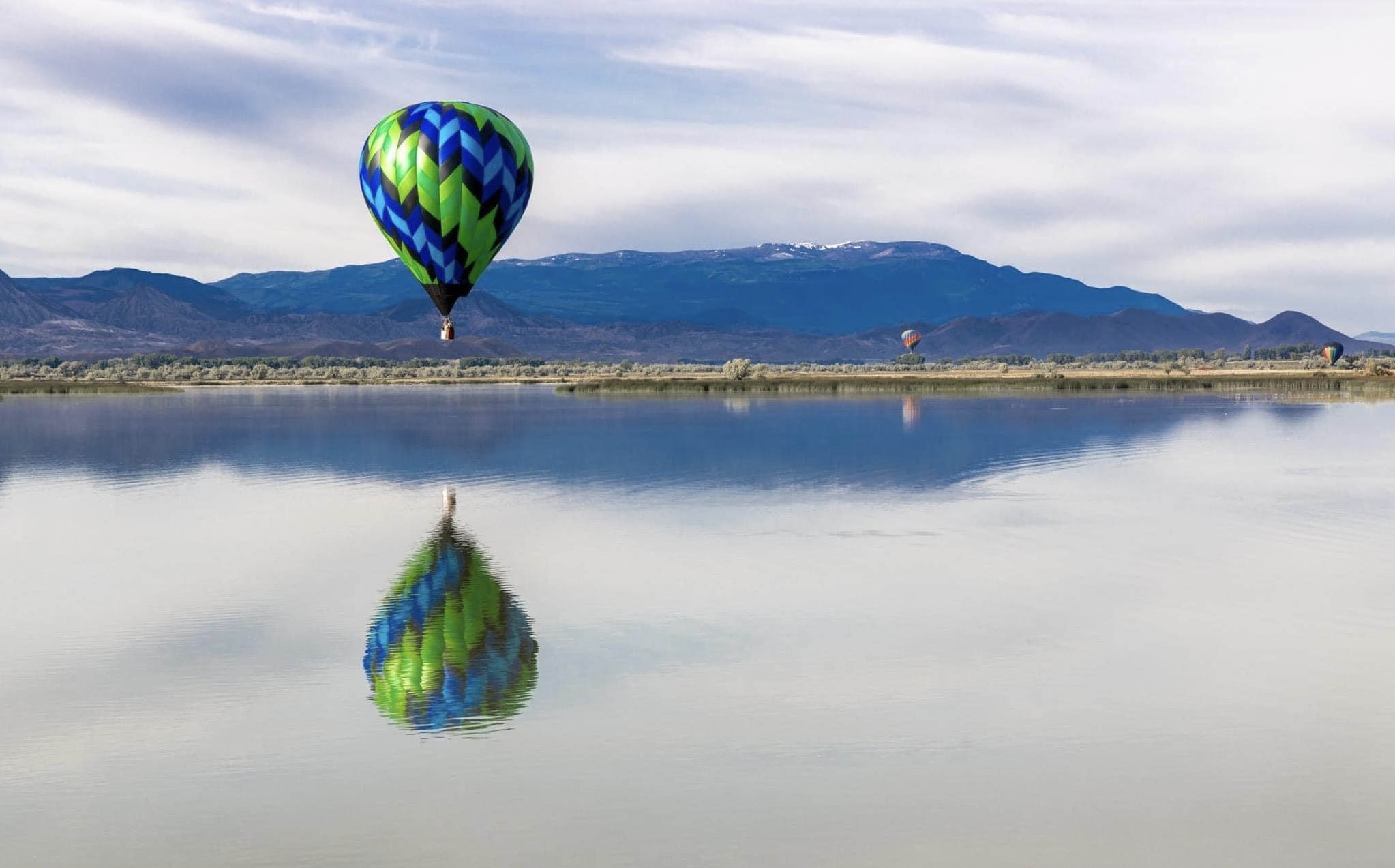 Hot air balloon floating over calm water with stunning reflection